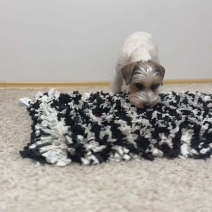 A small dog sniffing a black and white snuffle mat designed for mental stimulation.